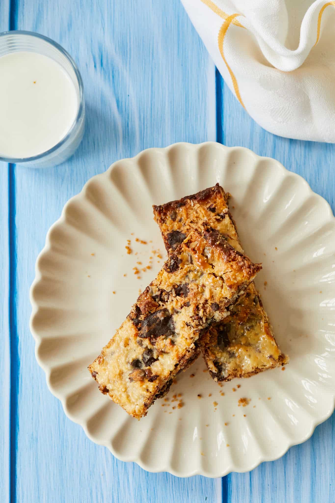 Two Magic Cookie Bars are served on a white plate, the top of the Magic Bars is covered in gooey, caramelized condensed milk.