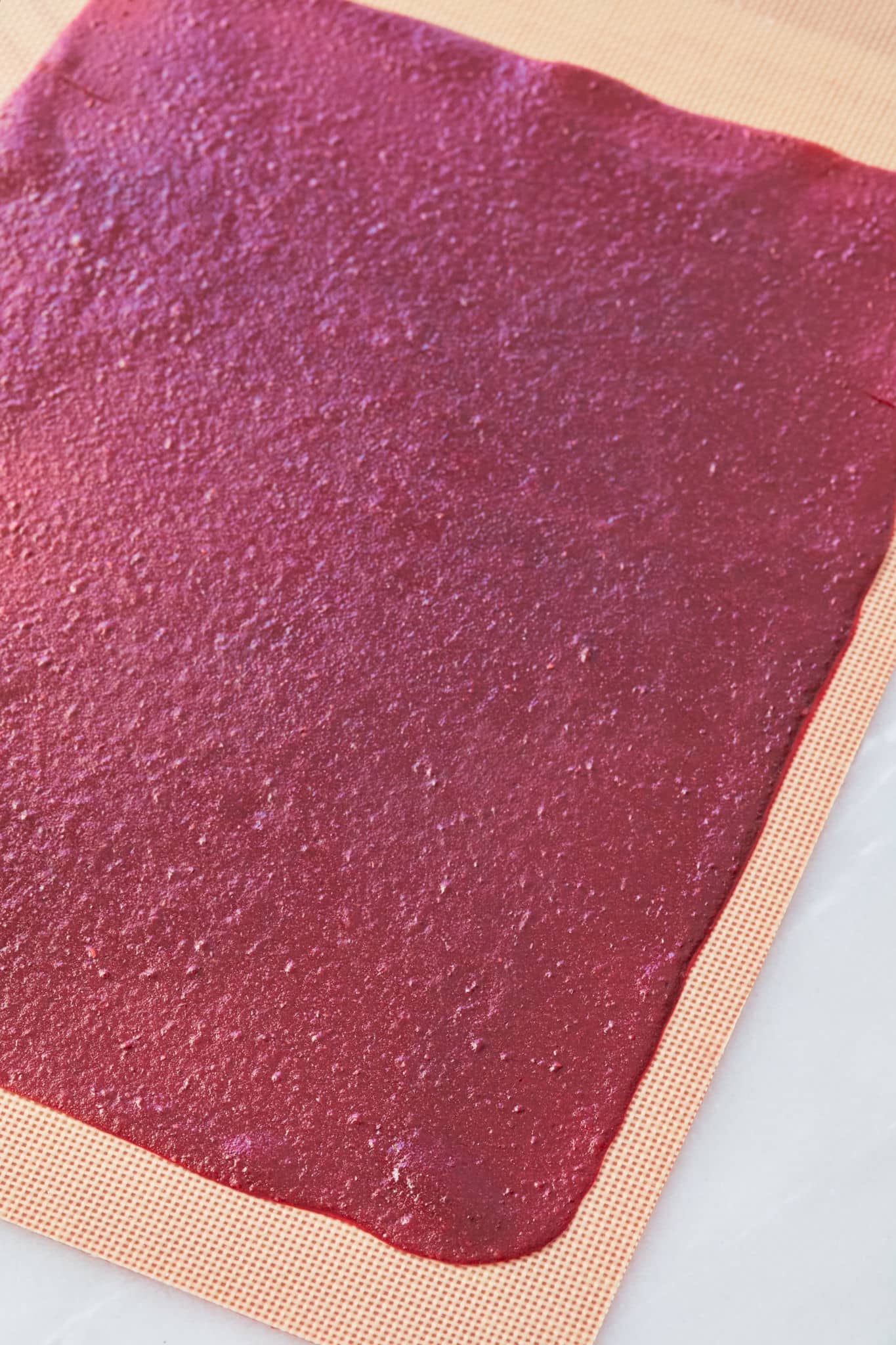 A thin layer of puree used to make raspberry leather is spread on a silicone baking sheet after baking.