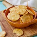 A bowl of homemade Ritz Crackers sit on a wood cutting board. They look crispy.