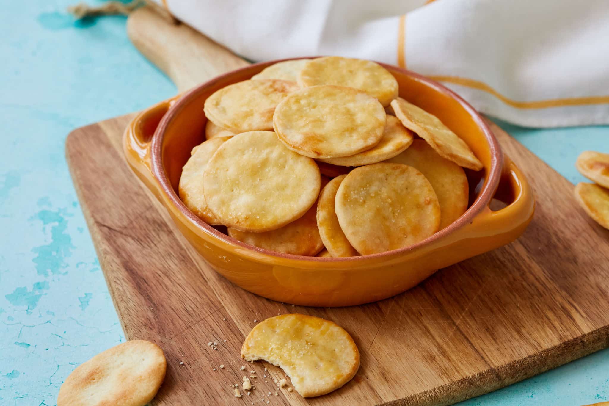 A bowl of homemade Ritz Crackers sit on a wood cutting board. They look crispy.