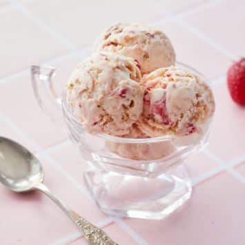 Strawberry Cheesecake Ice Cream in a bowl next to a spoon and strawberries