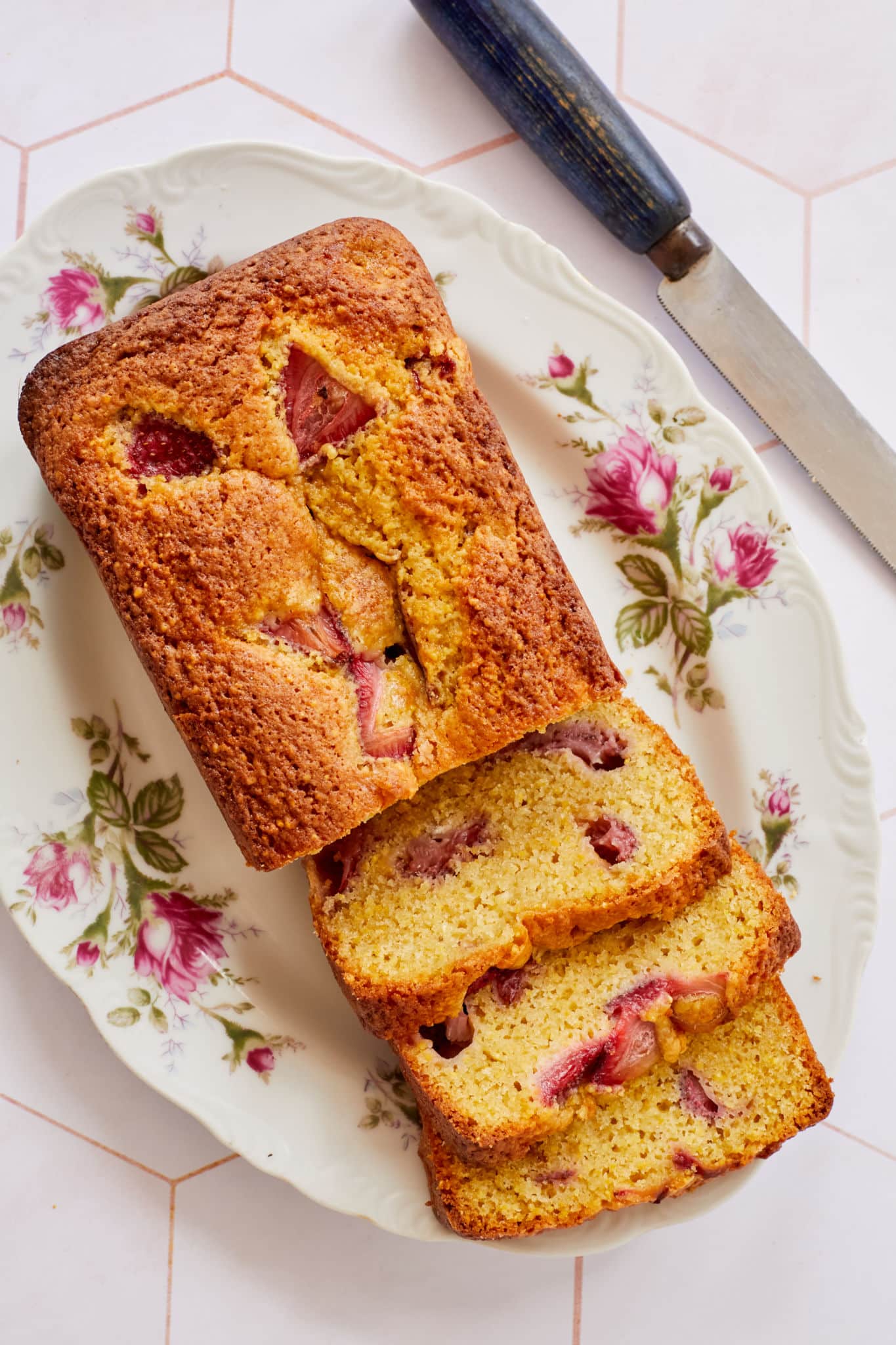A strawberry cornmeal quick bread is displayed on a white serving platter with pink roses.