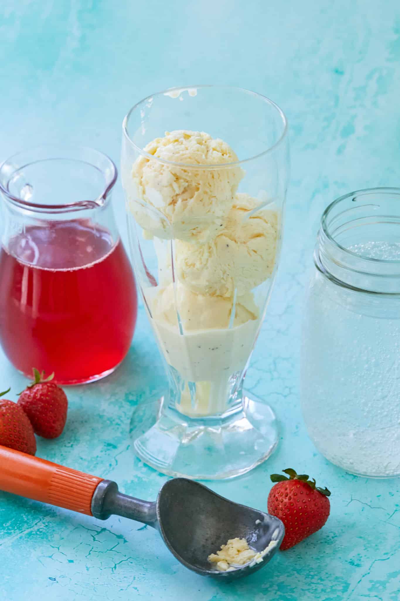 Ice cream in a glass next to strawberry syrup