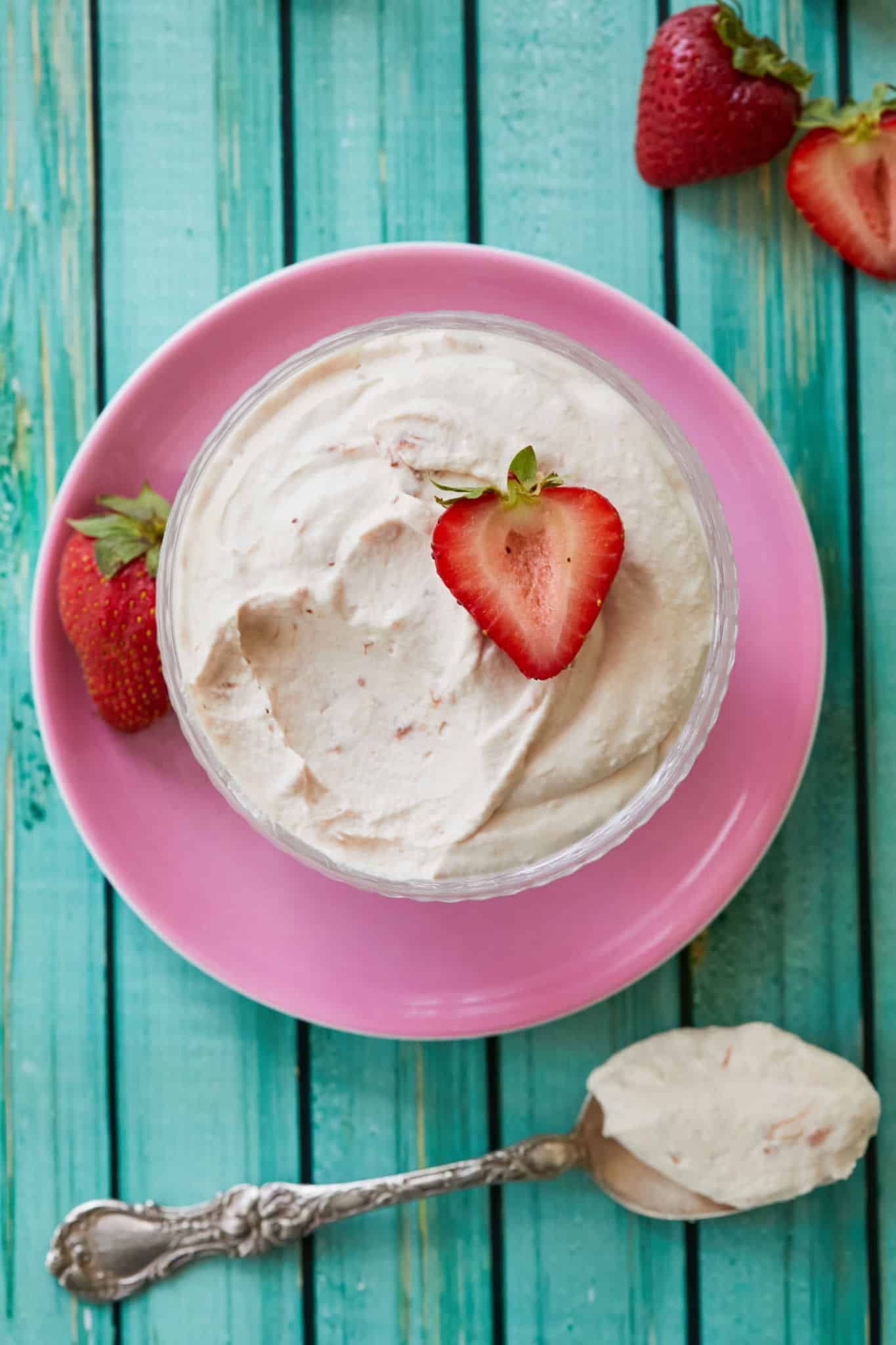 A bowl of homemade strawberry whipped cream sits on top of a pink plate with strawberries.