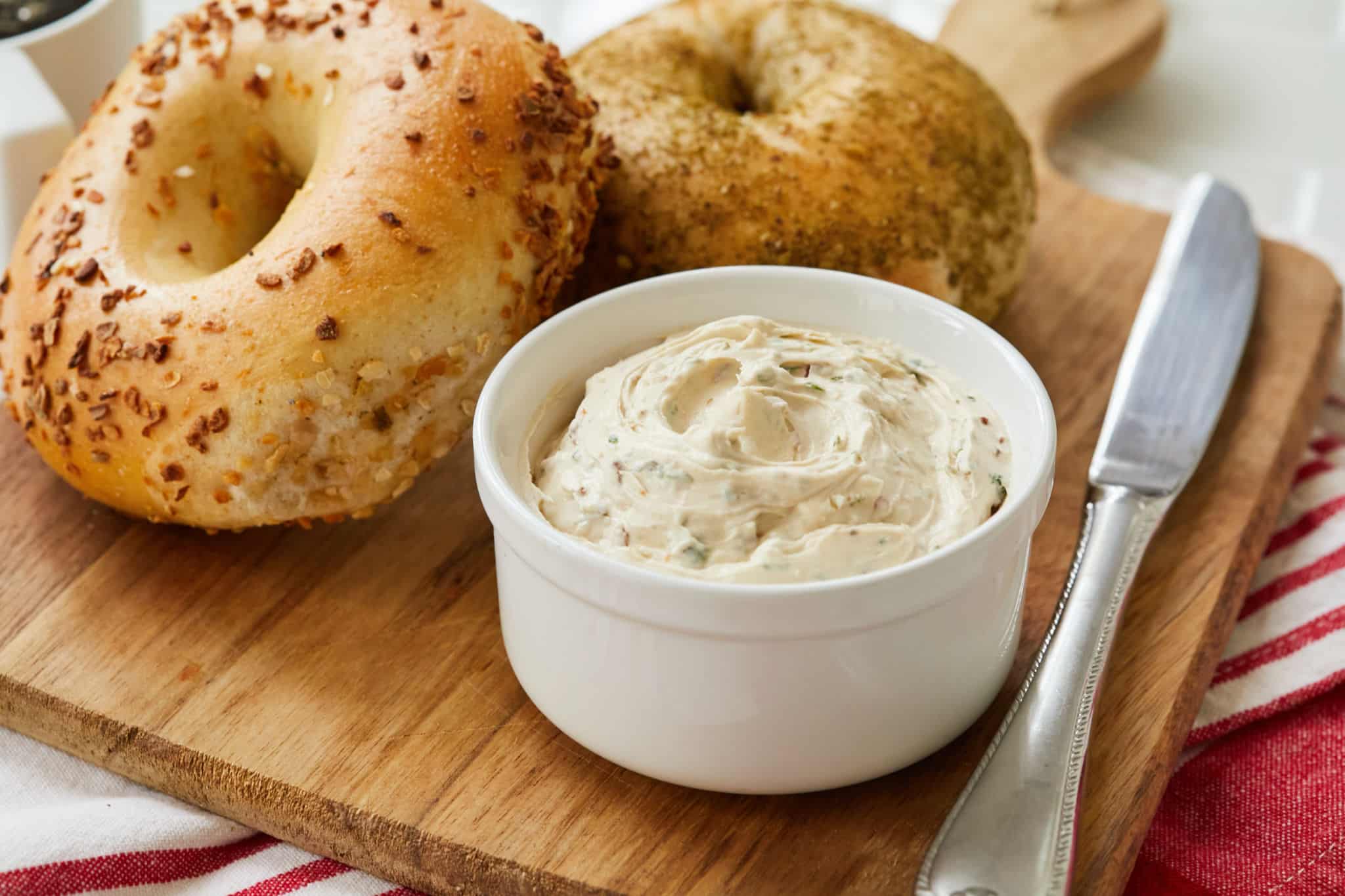 Homemade Sun-Dried Tomato Cream Cheese is served in a white dish next to a garlic bagel and a poppyseed bagel.