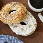Homemade Smoked Salmon Cream Cheese is smeared on an everything bagel next to a black cup of coffee