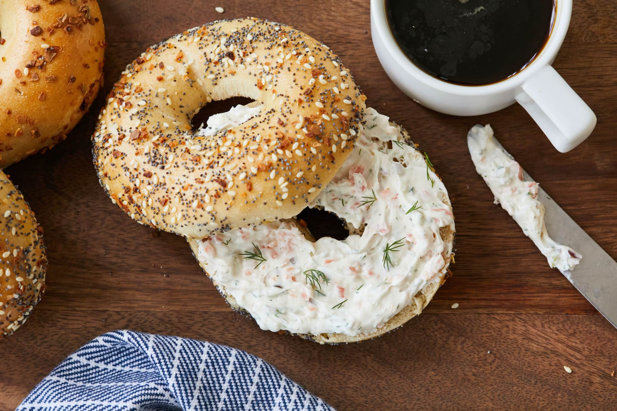 Homemade Smoked Salmon Cream Cheese is smeared on an everything bagel next to a black cup of coffee
