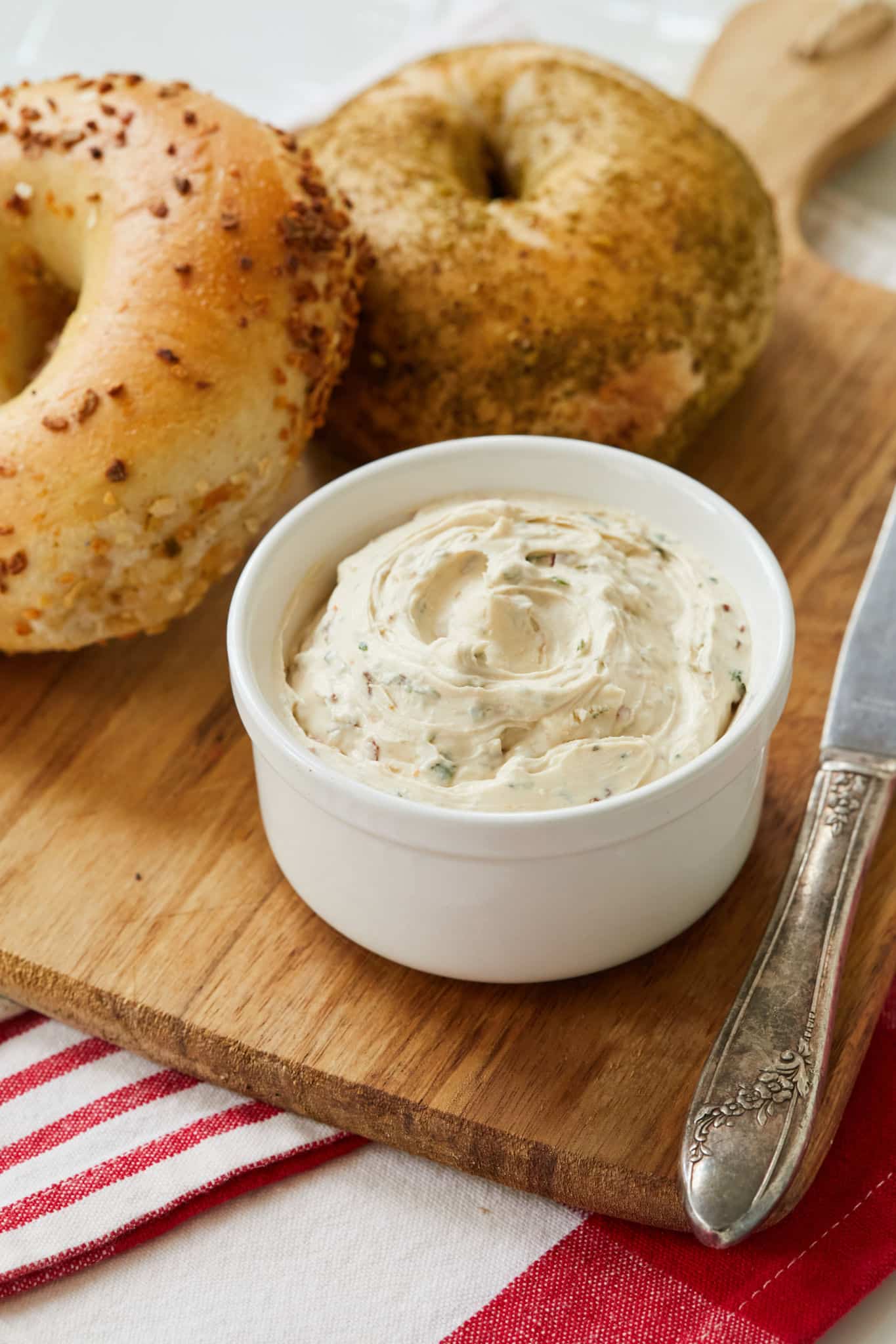 Homemade Sun-Dried Tomato Cream Cheese is served in a white dish next to a garlic bagel.