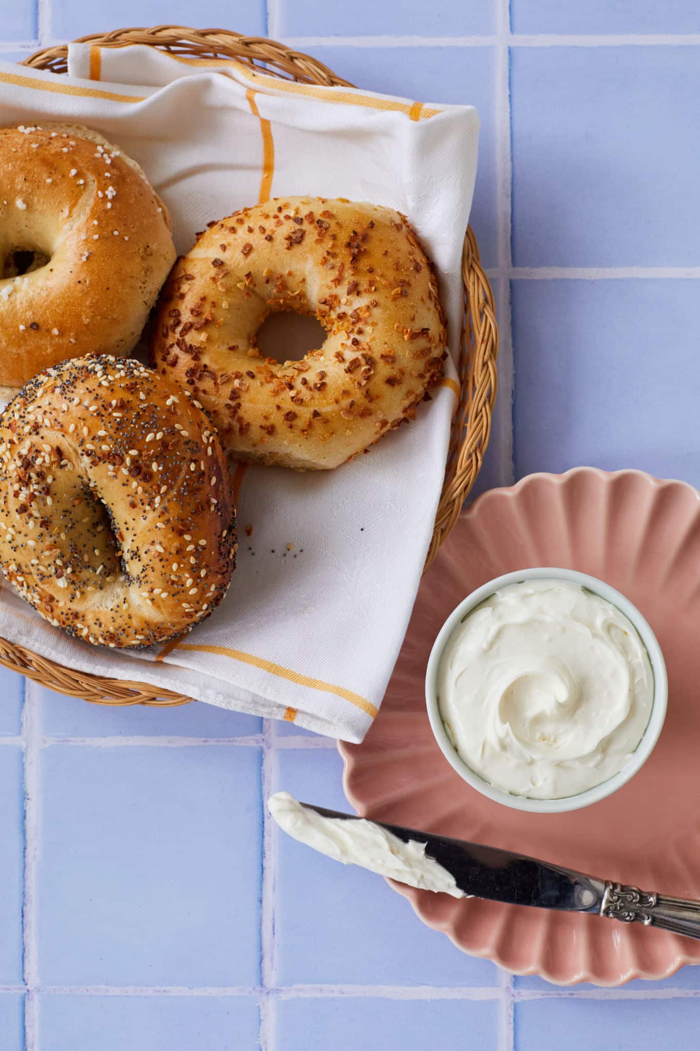 Homemade whipped cream cheese is served next to one salt bagel, one onion bagel, and one everything bagel.