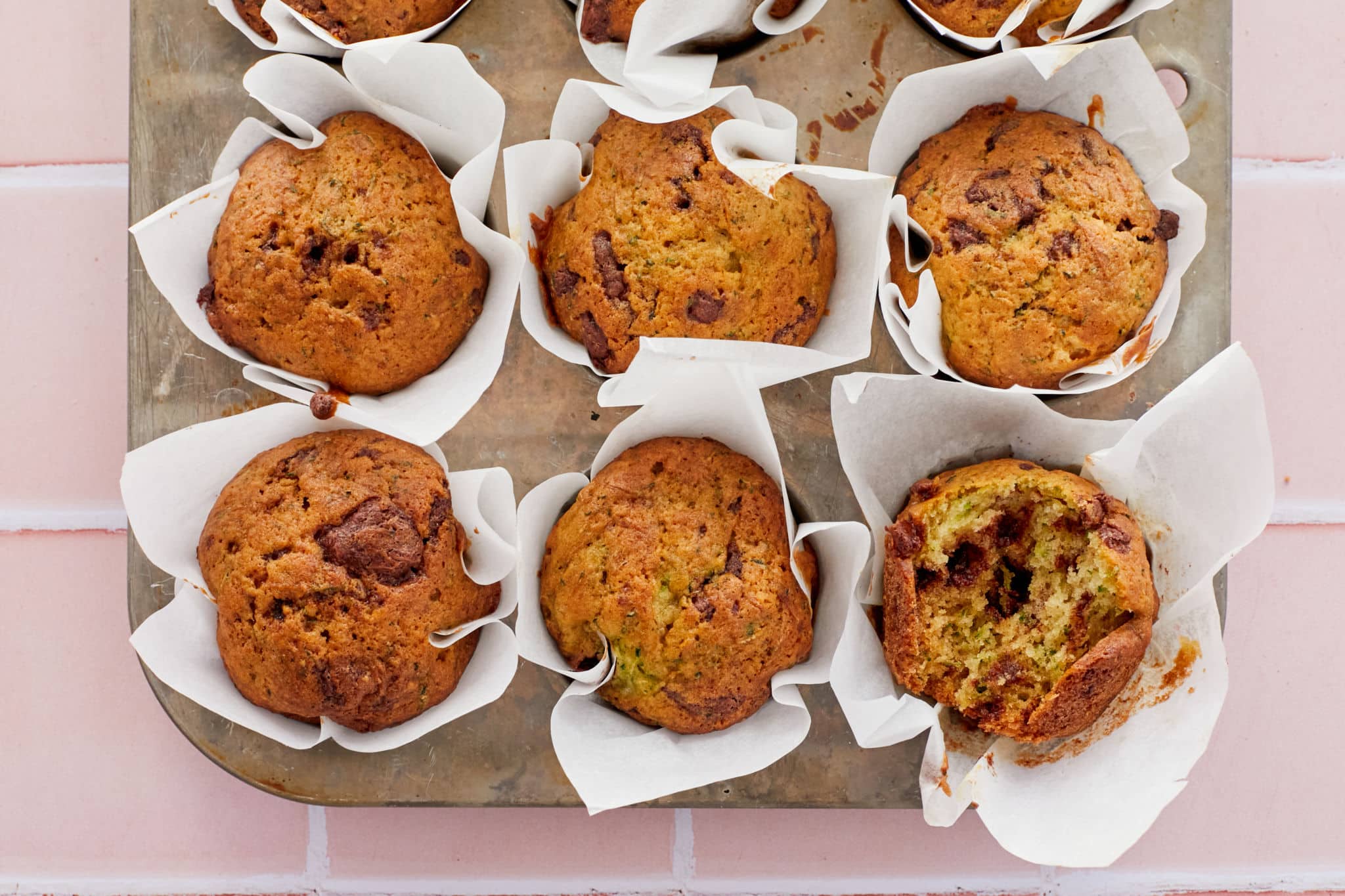Homemade Zucchini Chocolate Chip Muffins rest in a cupcake pan using parchment paper instead of cupcake wrappers.