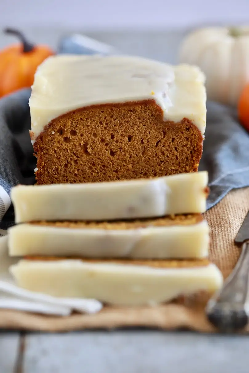 A loaf of pumpkin bread with a tight, pleasing crumb, is covered in a white glaze.