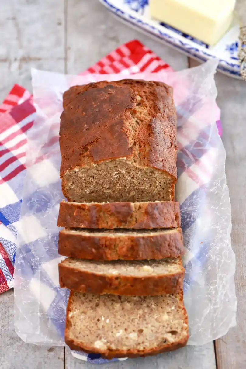 A moist banana bread sits on top of parchment paper with four slices cut from the loaf. 