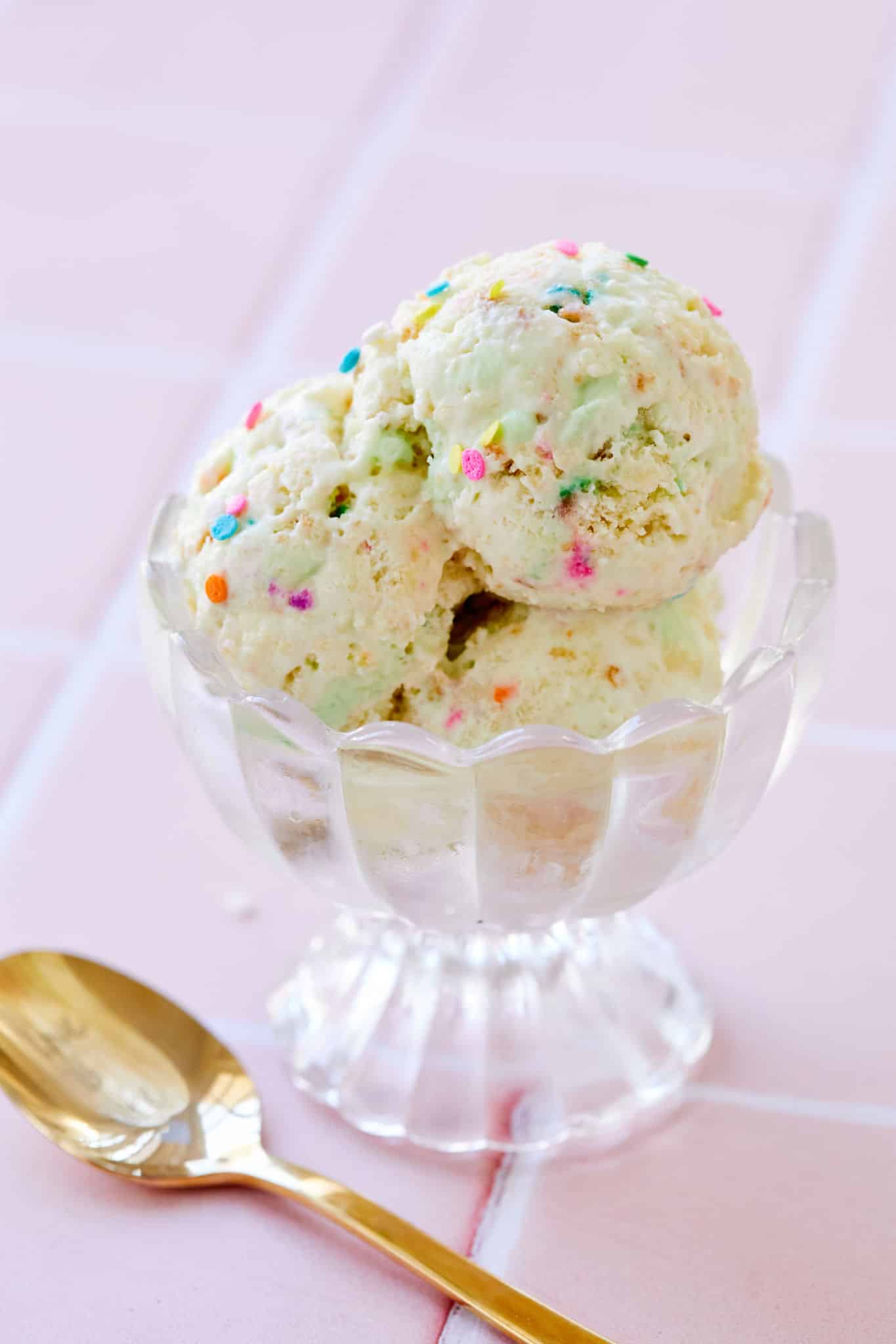 A bowl of ice cream with sprinkles next to a gold spoon