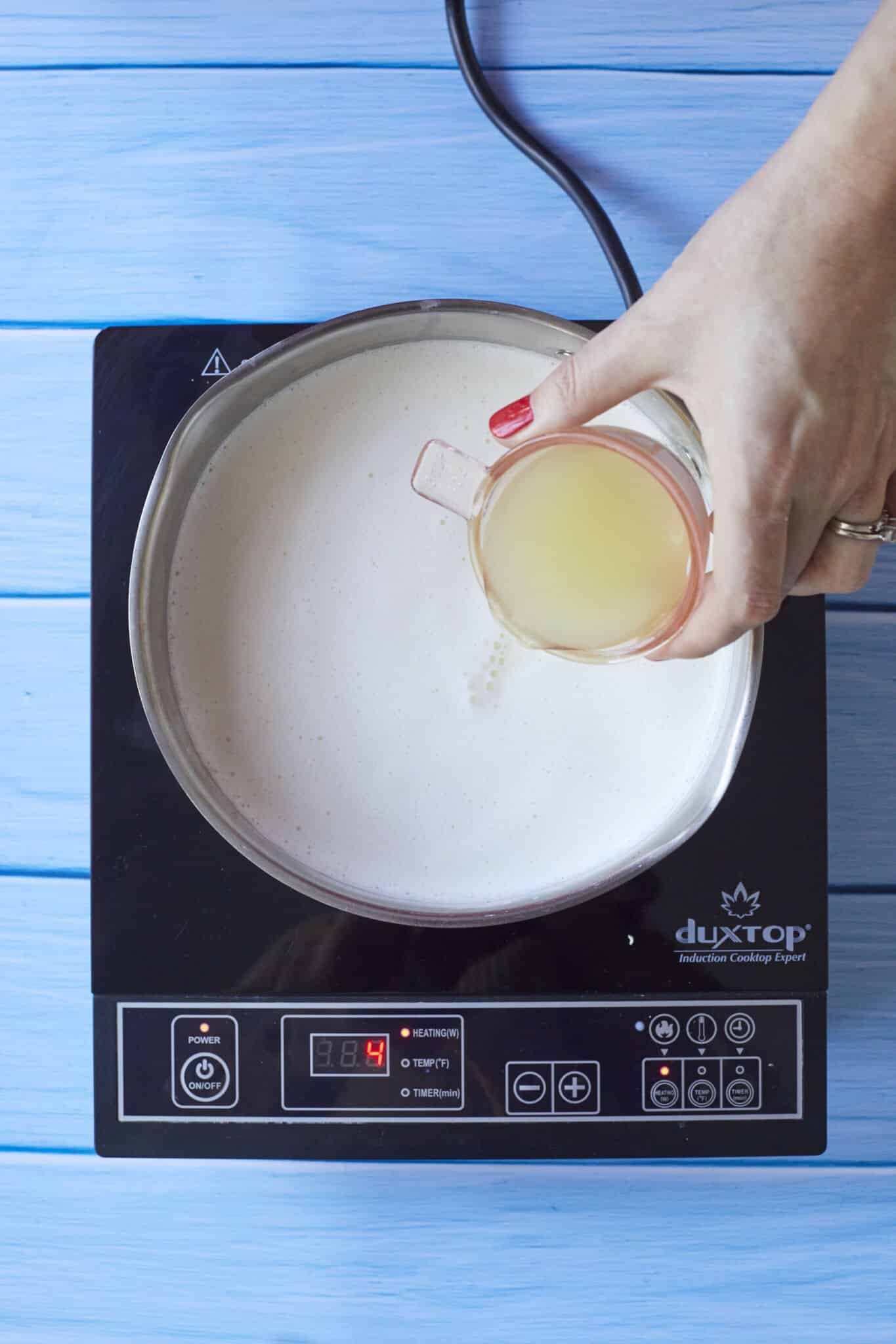 Adding lemon juice to the heated lemon posset mixture. 
