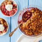 Two servings of healthy breakfast crisp are presented in two white bowls next to the berry crisp in the pie tin. There is a dollop of Greek yogurt on the two servings.