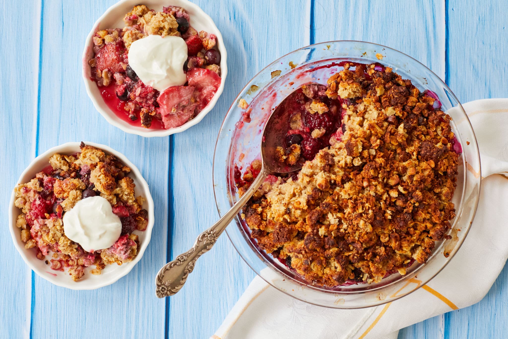 Two servings of healthy breakfast crisp are presented in two white bowls next to the berry crisp in the pie tin. There is a dollop of Greek yogurt on the two servings.