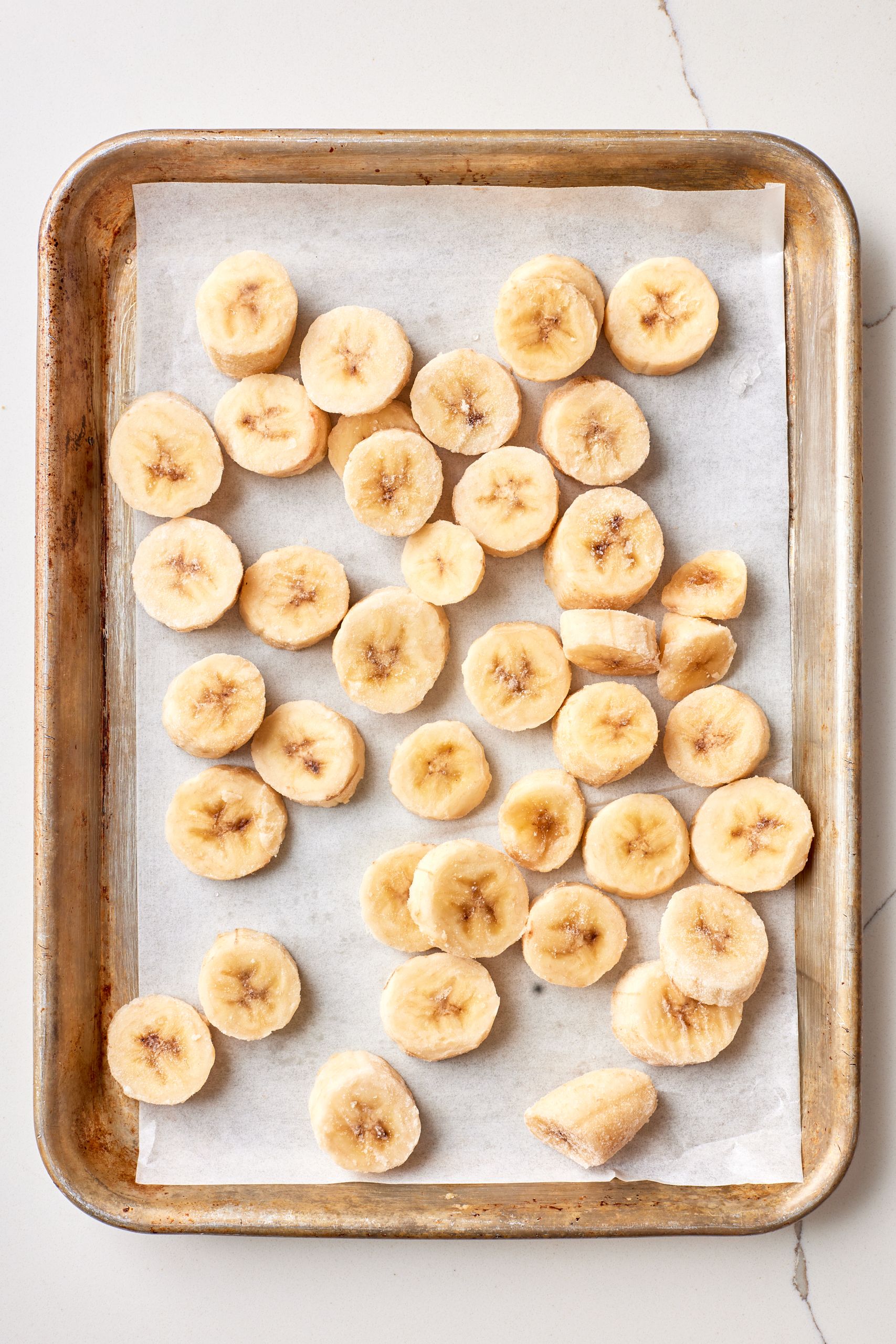 Step-by-step instructions on how to make healthy chocolate banana ice cream: slice and freeze bananas on a parchments-lined baking tray.