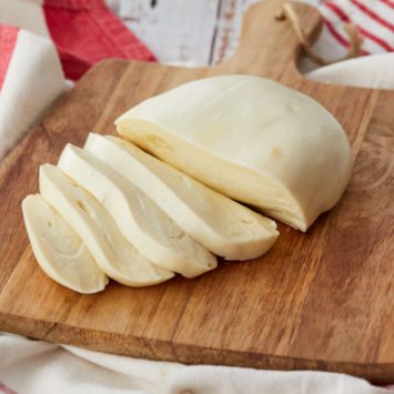 A ball of mozzarella cheese cut into slices on a board.