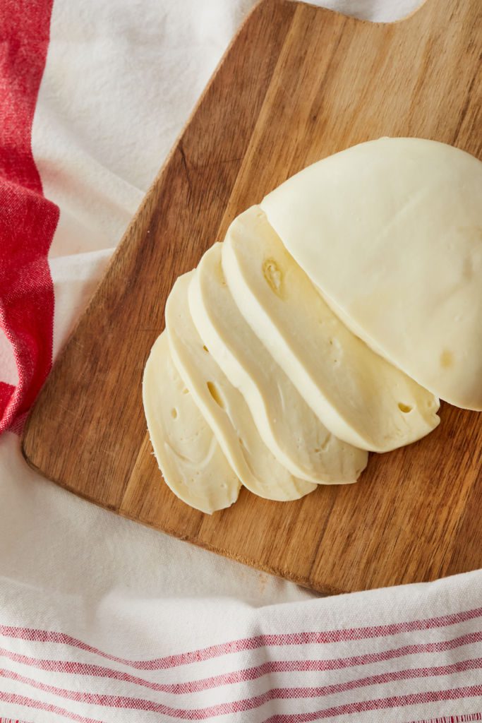 A ball of mozzarella cheese cut into slices on a board.