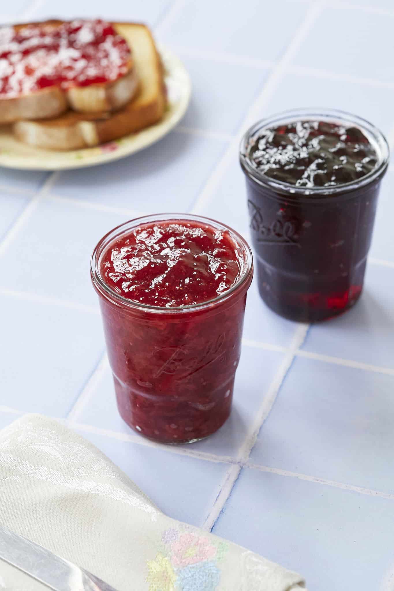 Two jars are next to each other, one is homemade jam, one is homemade jelly. 