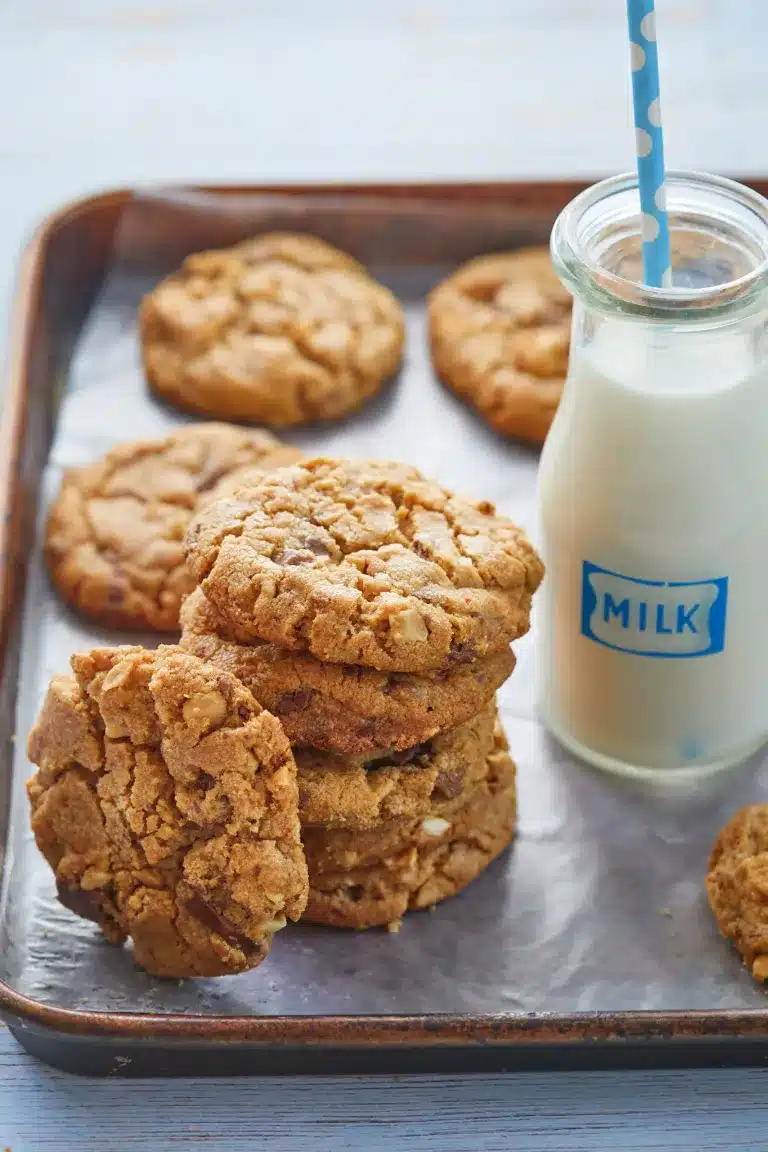 A stack of homemade peanut butter and chocolate cookies sit next to a glass of milk.