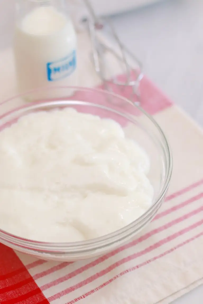 A bowl of whipped cream made with milk is on a table next to a glass with milk. Whipped Cream without heavy cream can be used in batter.