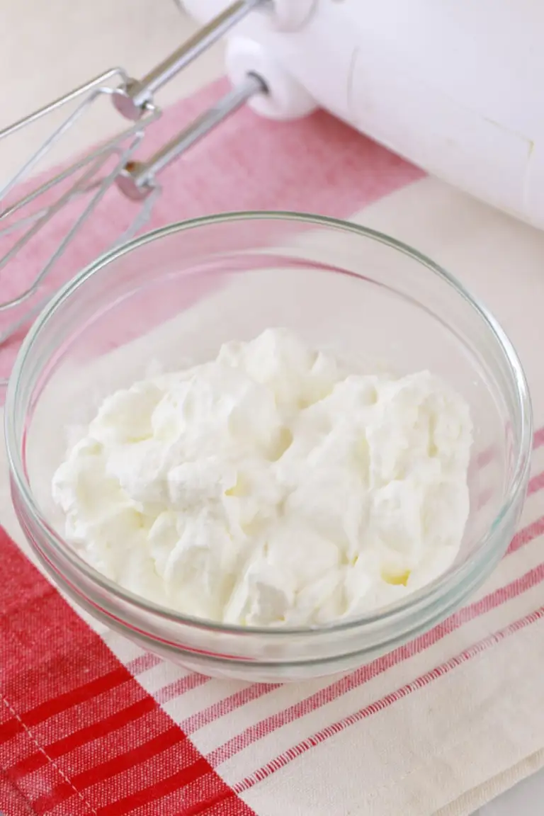 A bowl of classic homemade whipped cream sits next to a electric hand mixer