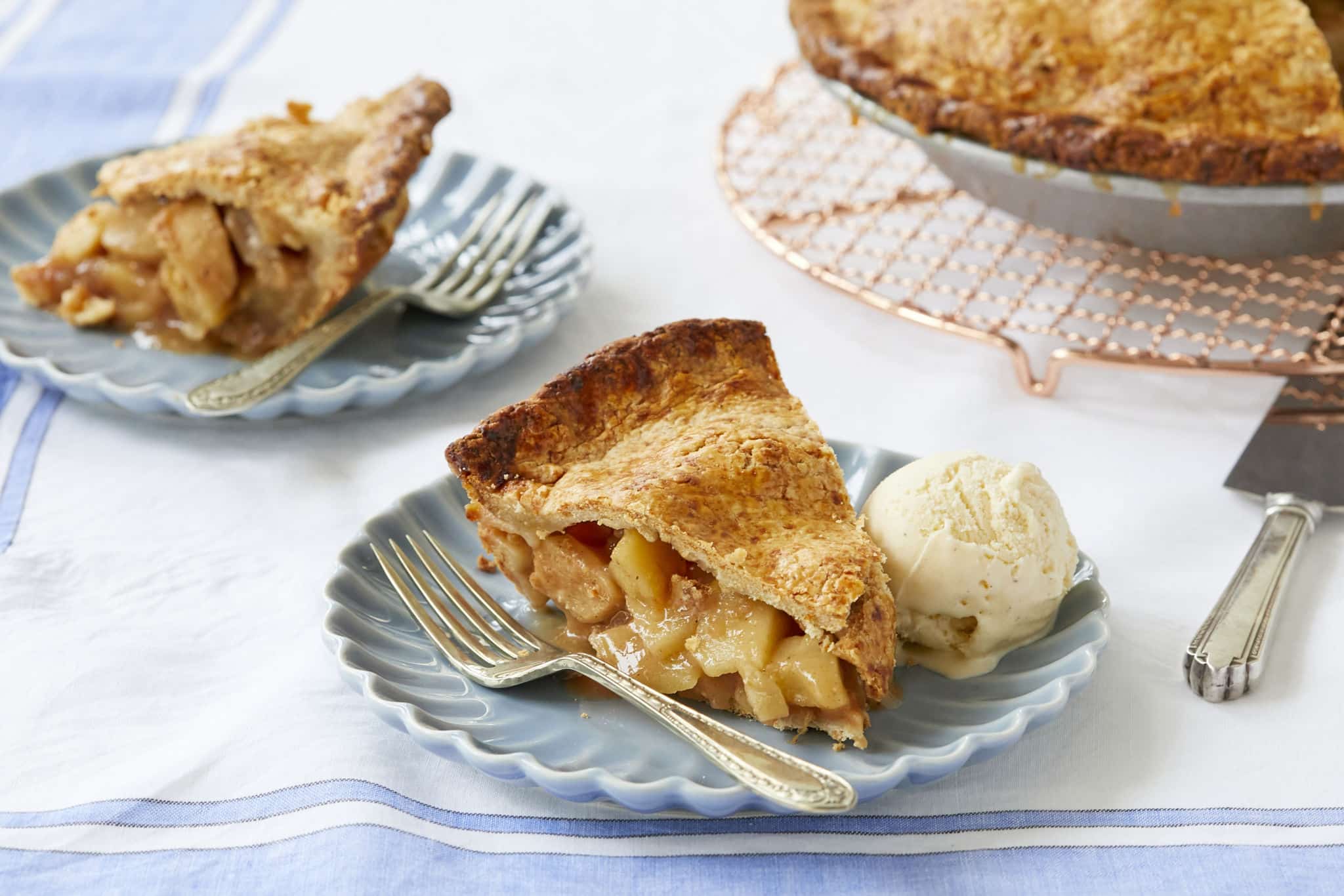 A slice of Apple Cheddar Pie is served on a dish with a scoop of vanilla ice cream. The apple pie filling is topped with a cheddar cheese crust.