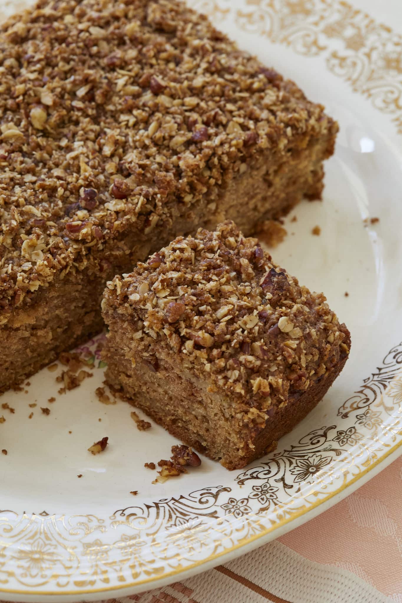 An apple snack cake is served on a dish. The streusel topping contains walnuts.