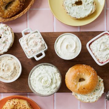 Whipped cream cheese with 5 amazing flavors served with bagels on a wooden board .