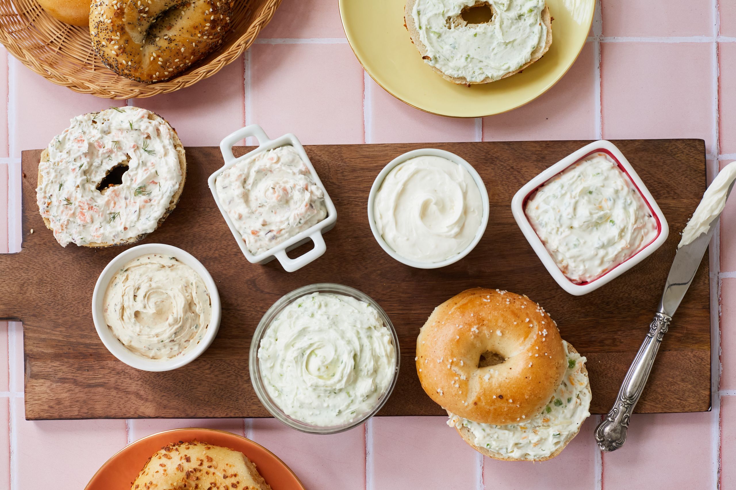 Whipped cream cheese with 5 amazing flavors served with bagels on a wooden board .