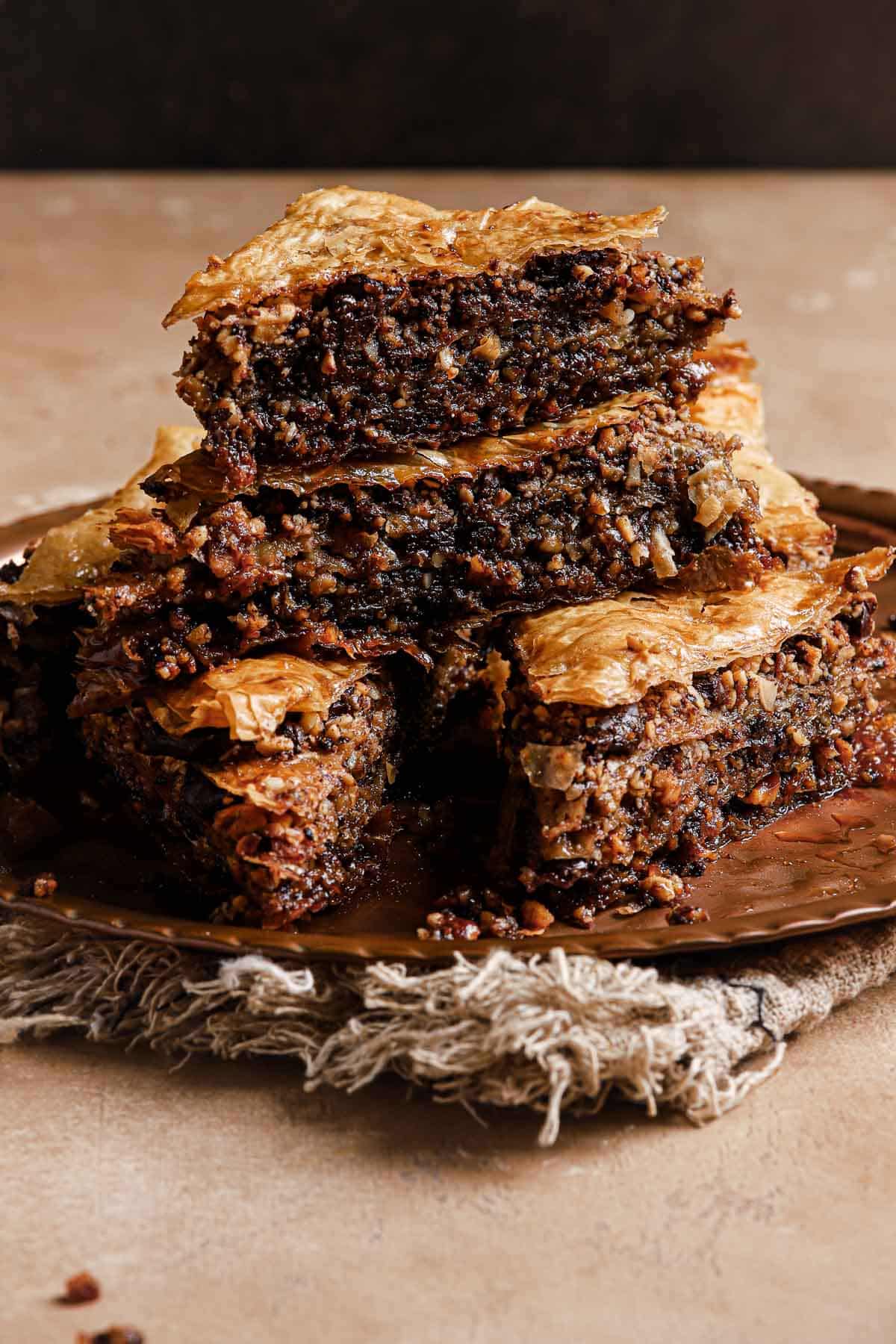 Triangular pieces of homemade chocolate baklava are stacked on a dish. The filo layers look golden brown and crispy while the chocolate baklava filling is deeply chocolatey and nutty. 