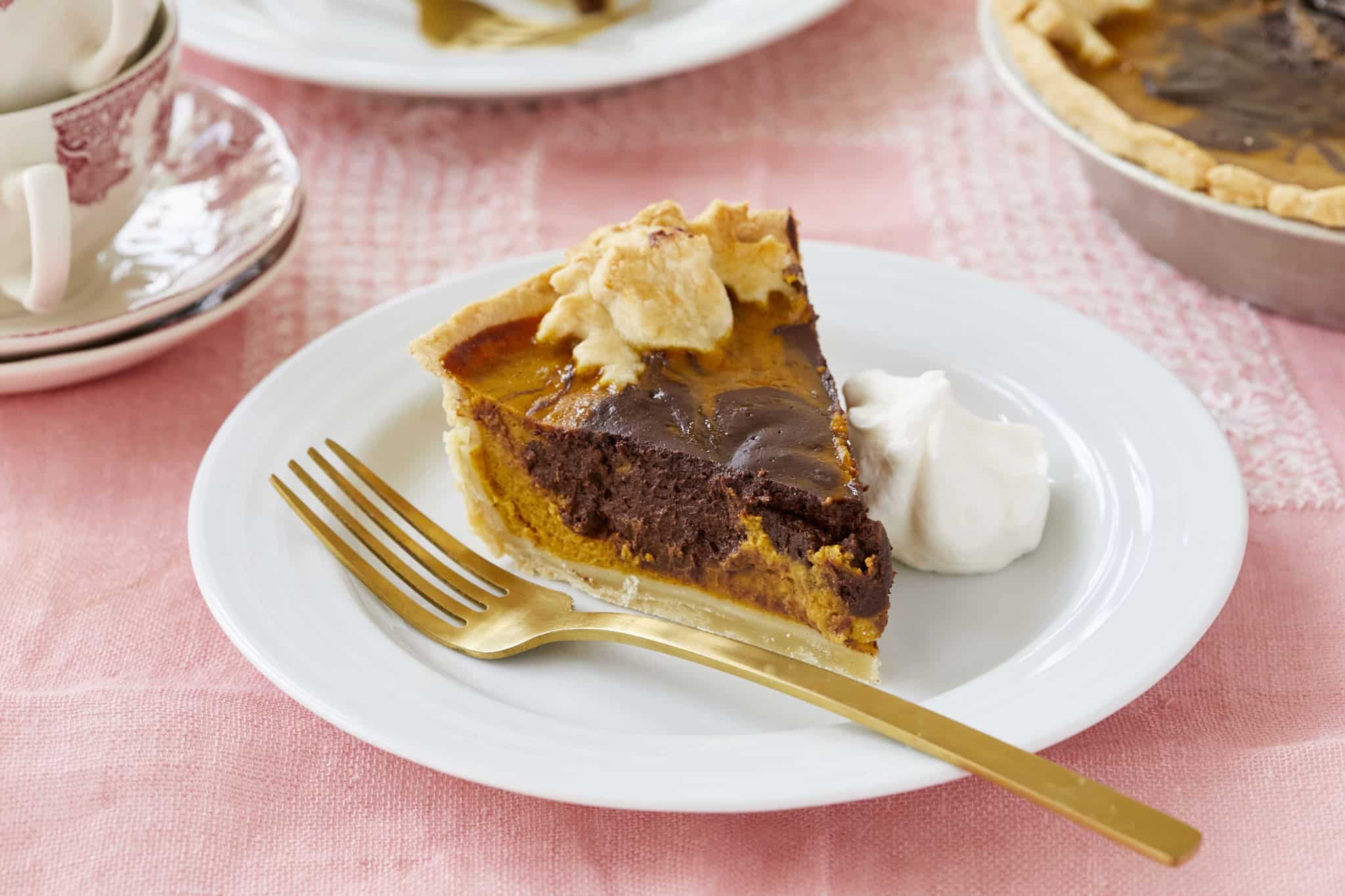 A slice of Chocolate Swirl Pumpkin Pie is served on a white dish with a dollop of homemade whipped cream on the side. Semisweet chocolate is swirled throughout the pumpkin filling.