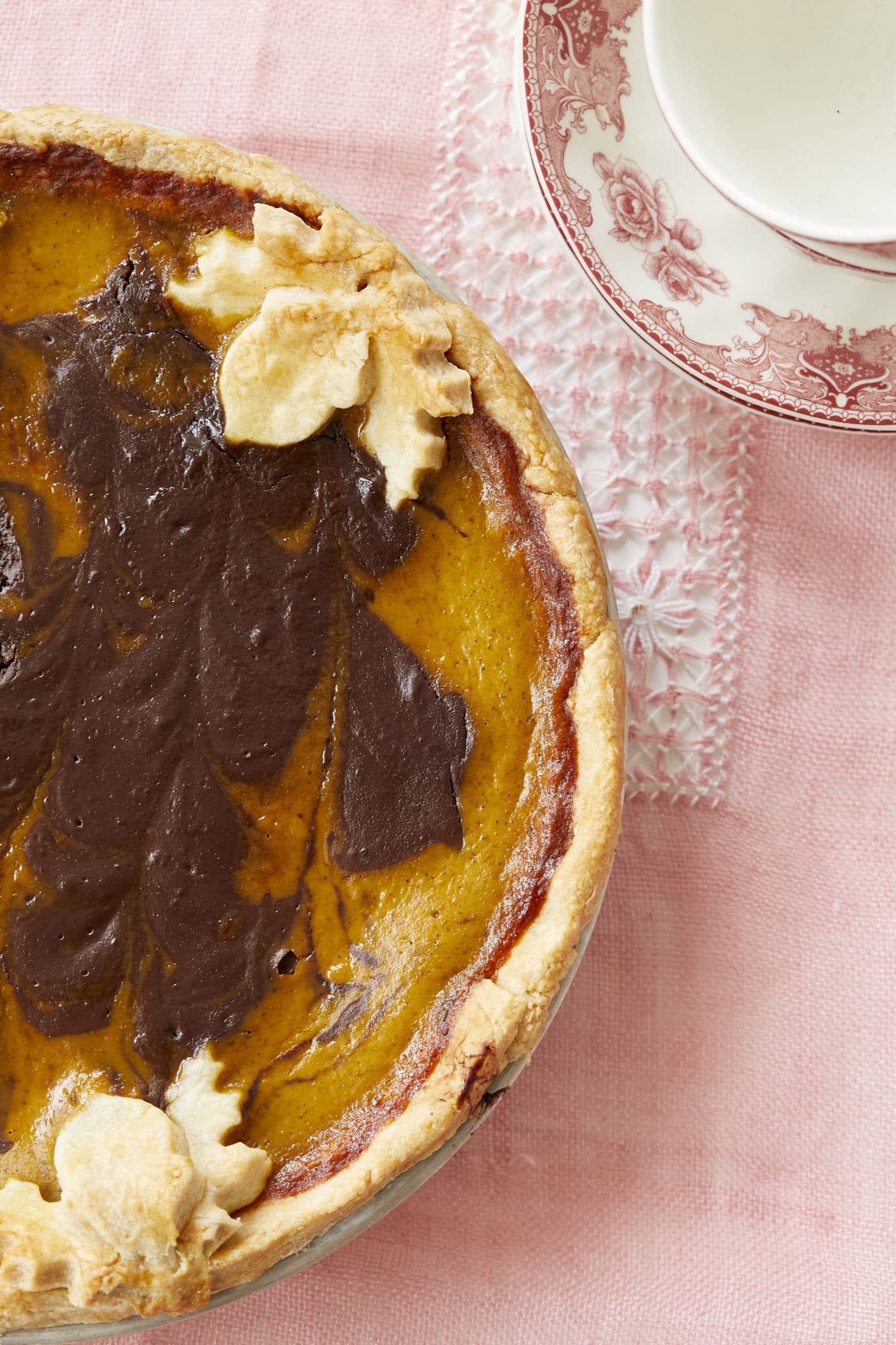 A close-up image of the Chocolate Swirl Pumpkin Pie, taken from over head, shows the semisweet chocolate swirled in with the pumpkin pie filling. The homemade pie crust is light brown and there are leaf-shaped pieces of pie crust.