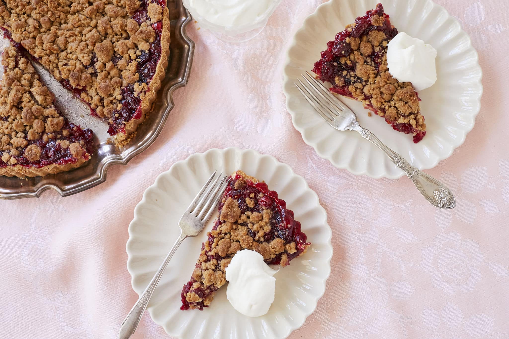 Two slices of homemade Cranberry Orange Crumb Tart are served on white dishes with a dollop of homemade whipped cream.