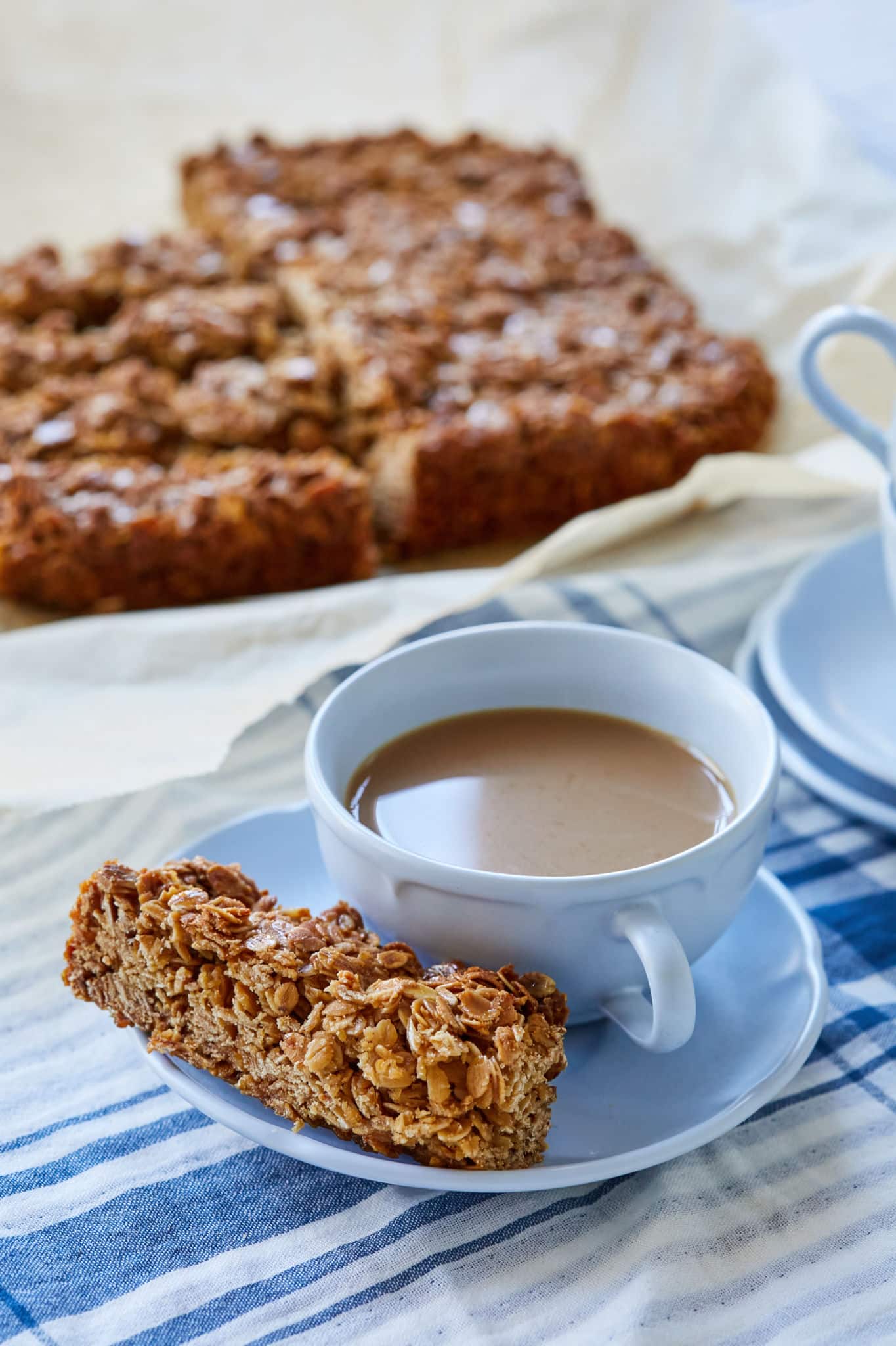 A bar of Irish Flapjacks is served next to a hot cup of tea with milk. 