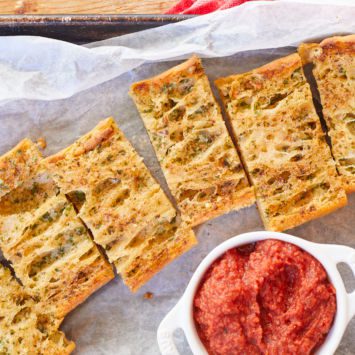 Homemade garlic bread from scratch is cut up into pieces and served alongside homemade pizza sauce.