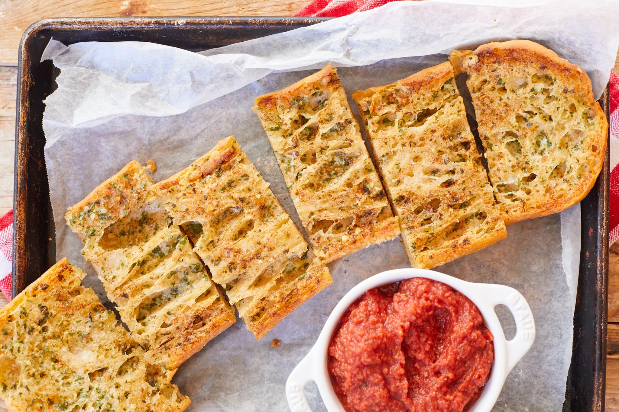 Homemade garlic bread from scratch is cut up into pieces and served alongside homemade pizza sauce.