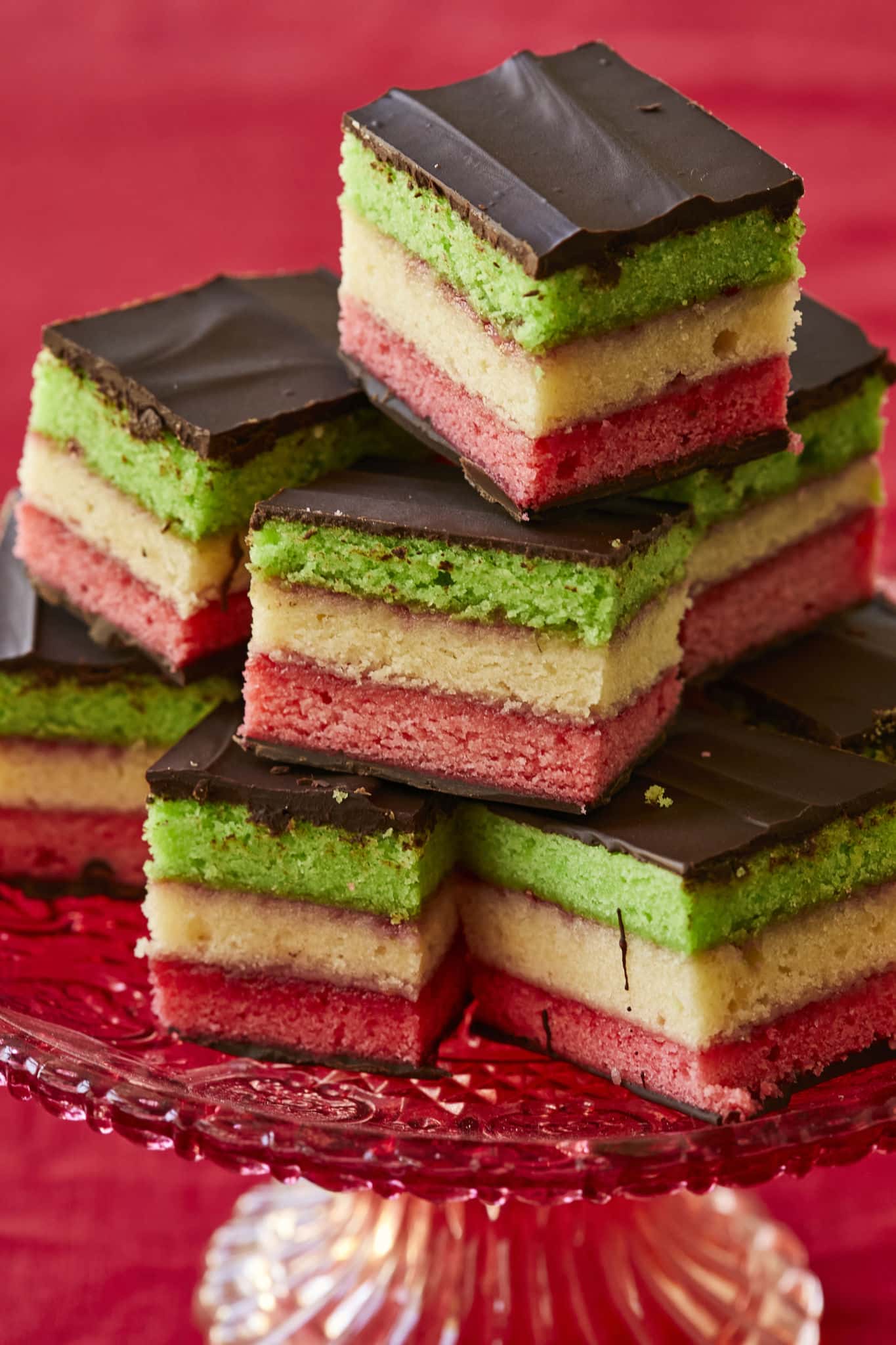 A closeup image of Italian Rainbow cookies show layers of multi-colored almond cake, sandwiched between two layers of chocolate.