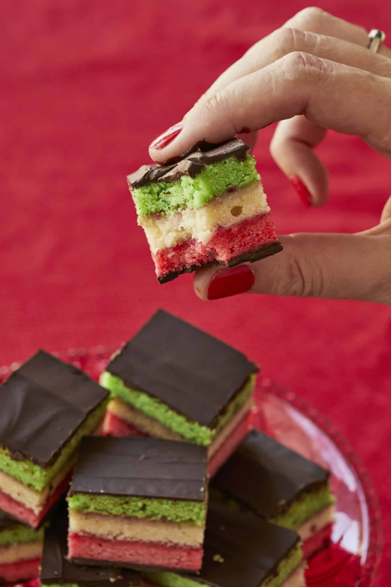 A bite is taken out of one Rainbow Cookie, showing the tricolor structure. In between the layers of cake is raspberry jam.
