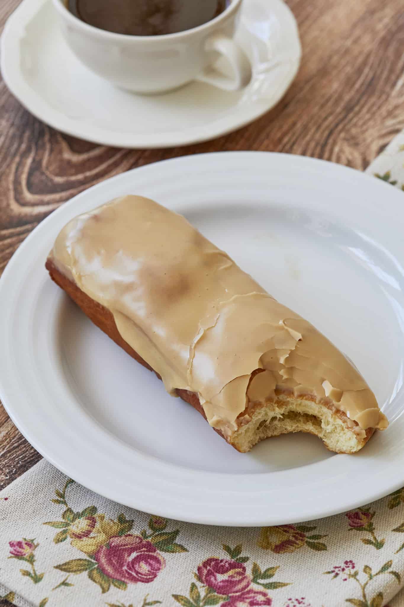 A bite is taken out of the long, log-shaped donut with maple glaze.