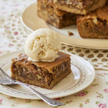 A scoop of vanilla ice cream is served on top of a homemade Maple Pecan Blondie. The center of the blondie looks chewy and moist with peaks of chopped up, toasted pecans
