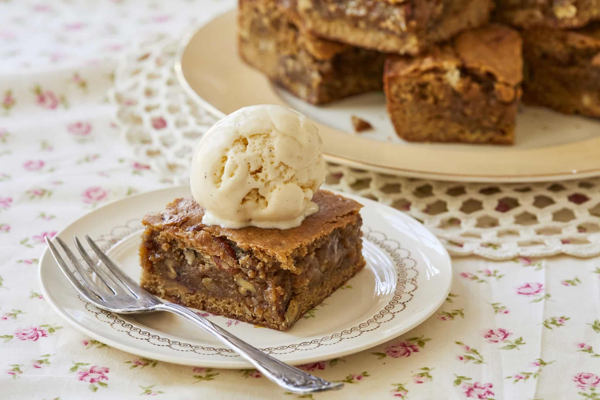 A scoop of vanilla ice cream is served on top of a homemade Maple Pecan Blondie. The center of the blondie looks chewy and moist with peaks of chopped up, toasted pecans