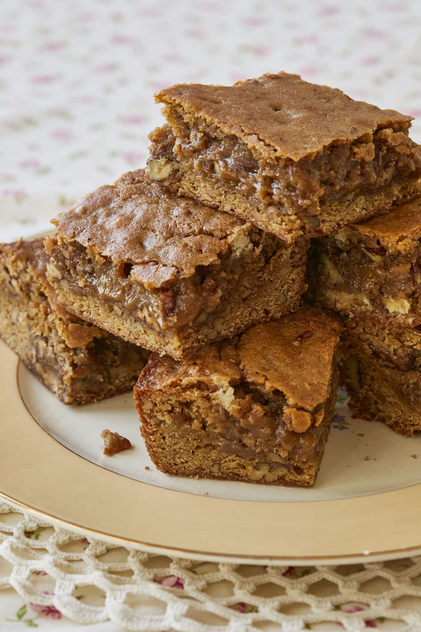 A batch of maple blondies are stacked on each other and a serving dish. There are toasted pecans in the blondies.