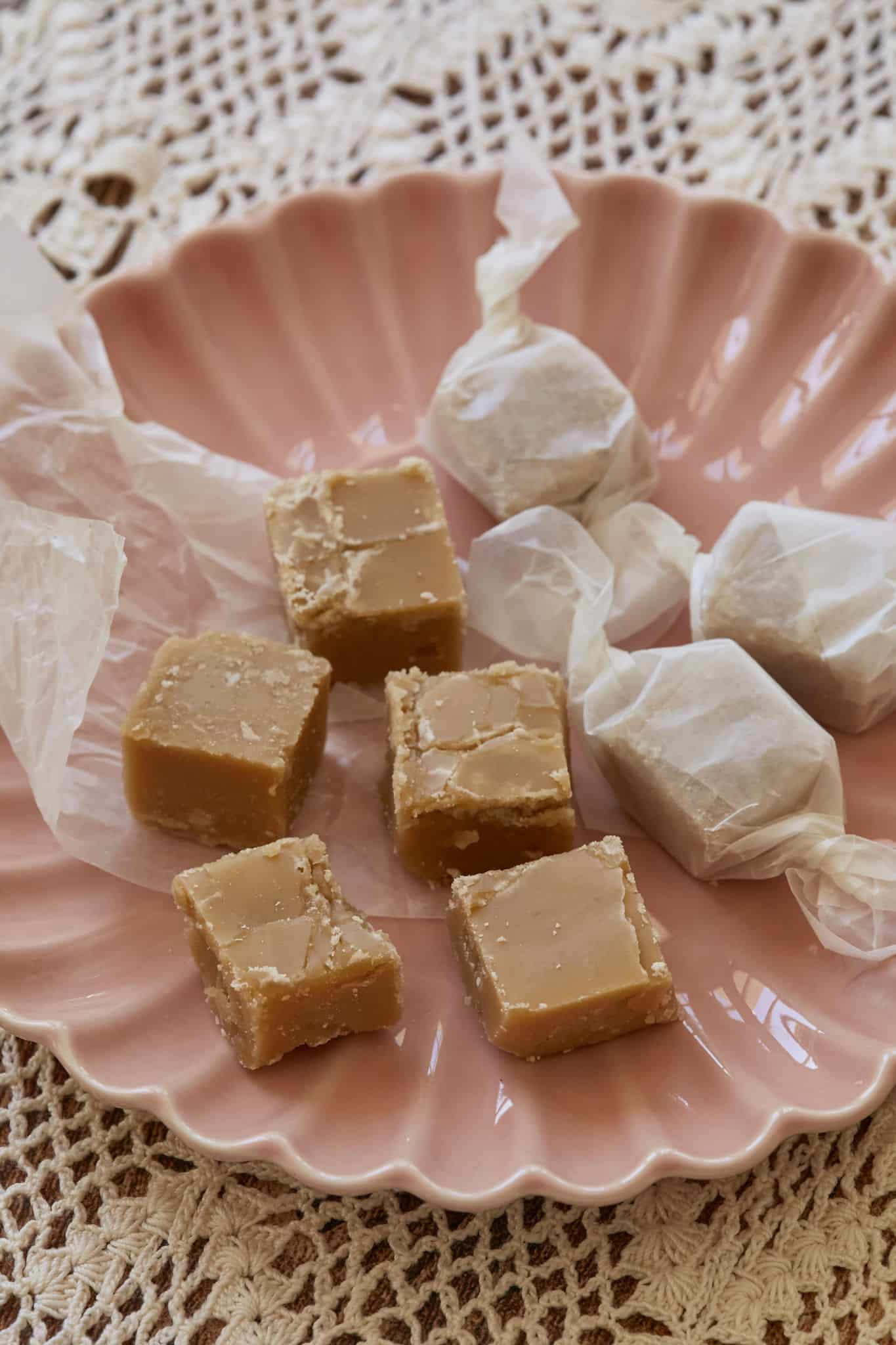 Square homemade candy made with maple syrup are served on a pink dish. The homemade candy is wrapped in parchment paper