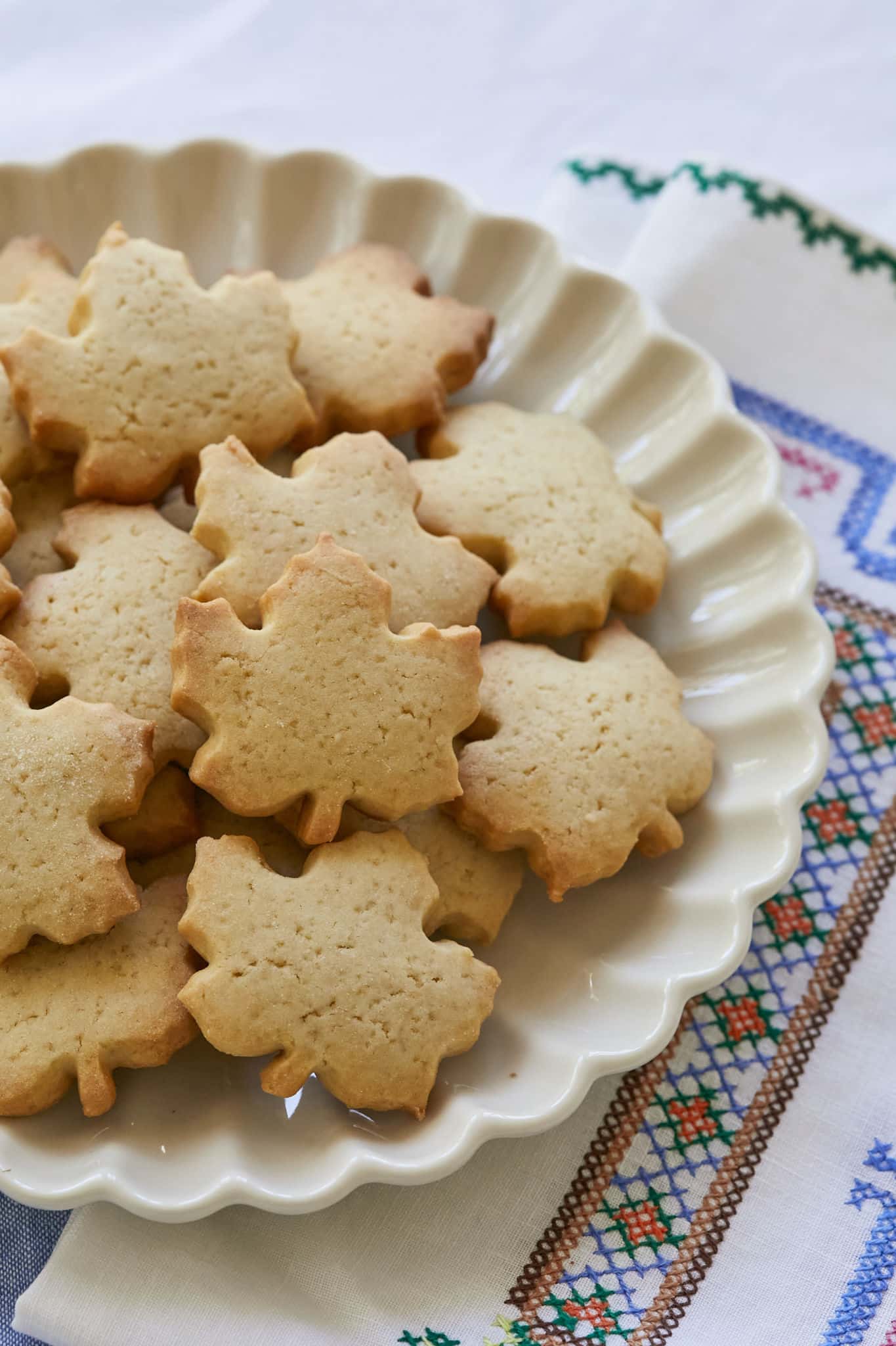 Maple cookies, cut in the shape of a maple leaf, are served on a white scalloped dish.