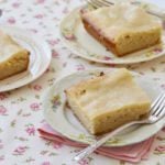 Three pieces of maple gooey butter cake on individual plates with forks, on a floral tablecloth.