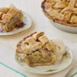 Homemade pear pie is sliced and served on two plates next to the pie remaining in the pie dish. It is served alongside homemade vanilla ice cream.