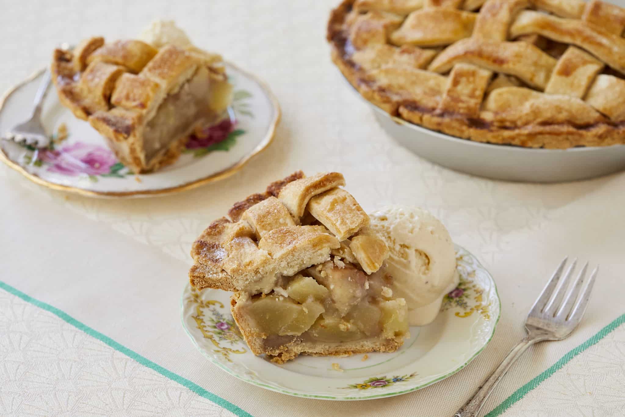 Homemade pear pie is sliced and served on two plates next to the pie remaining in the pie dish. It is served alongside homemade vanilla ice cream.