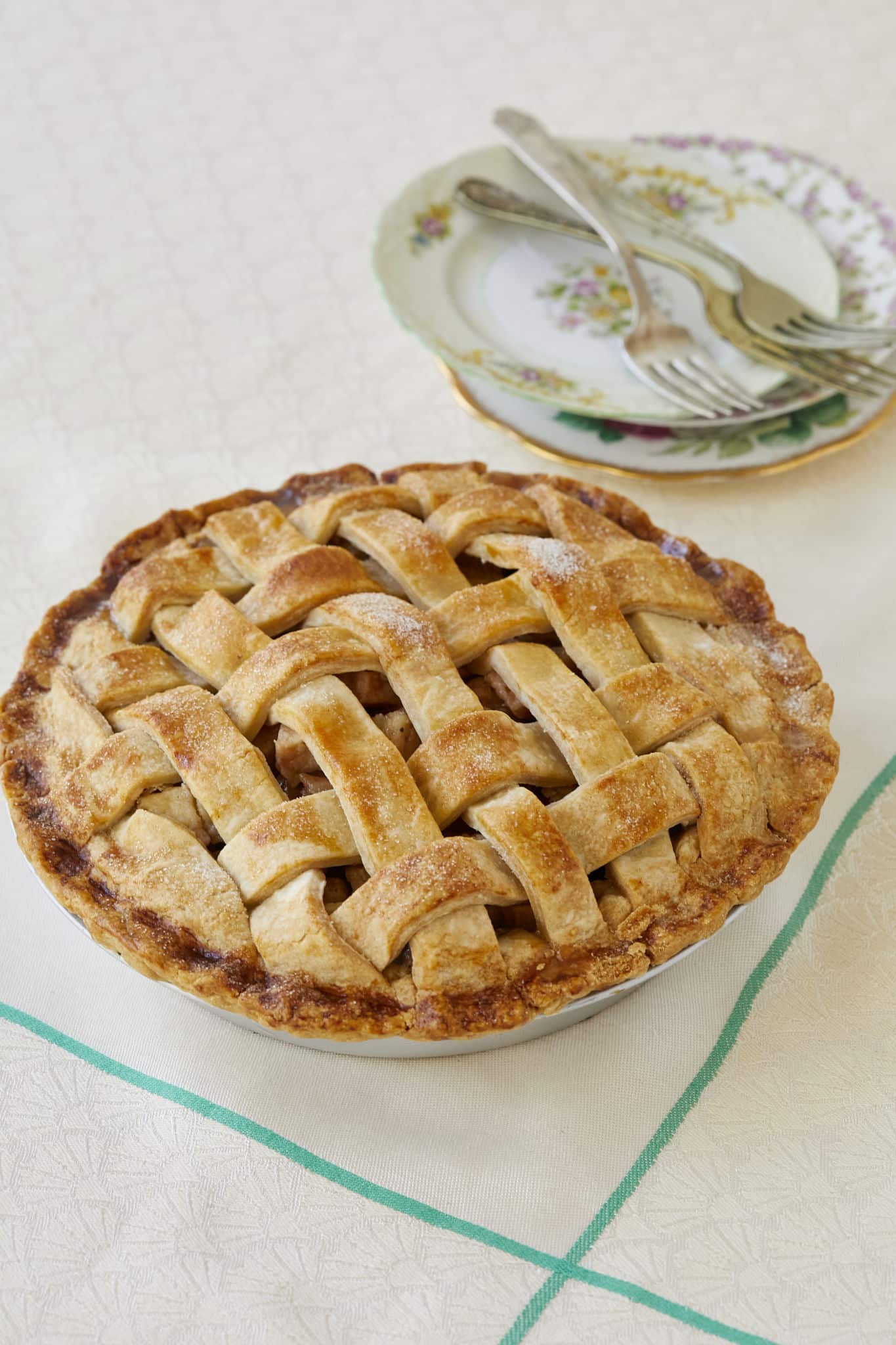Homemade fresh pear pie is displayed on a white table cloth. The homemade pie has a lattice topping.